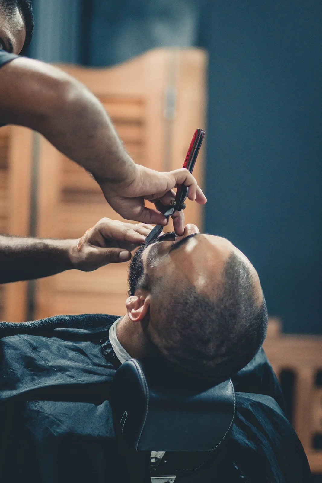 Detalle de barbero perfilando la barba de un cliente con navaja