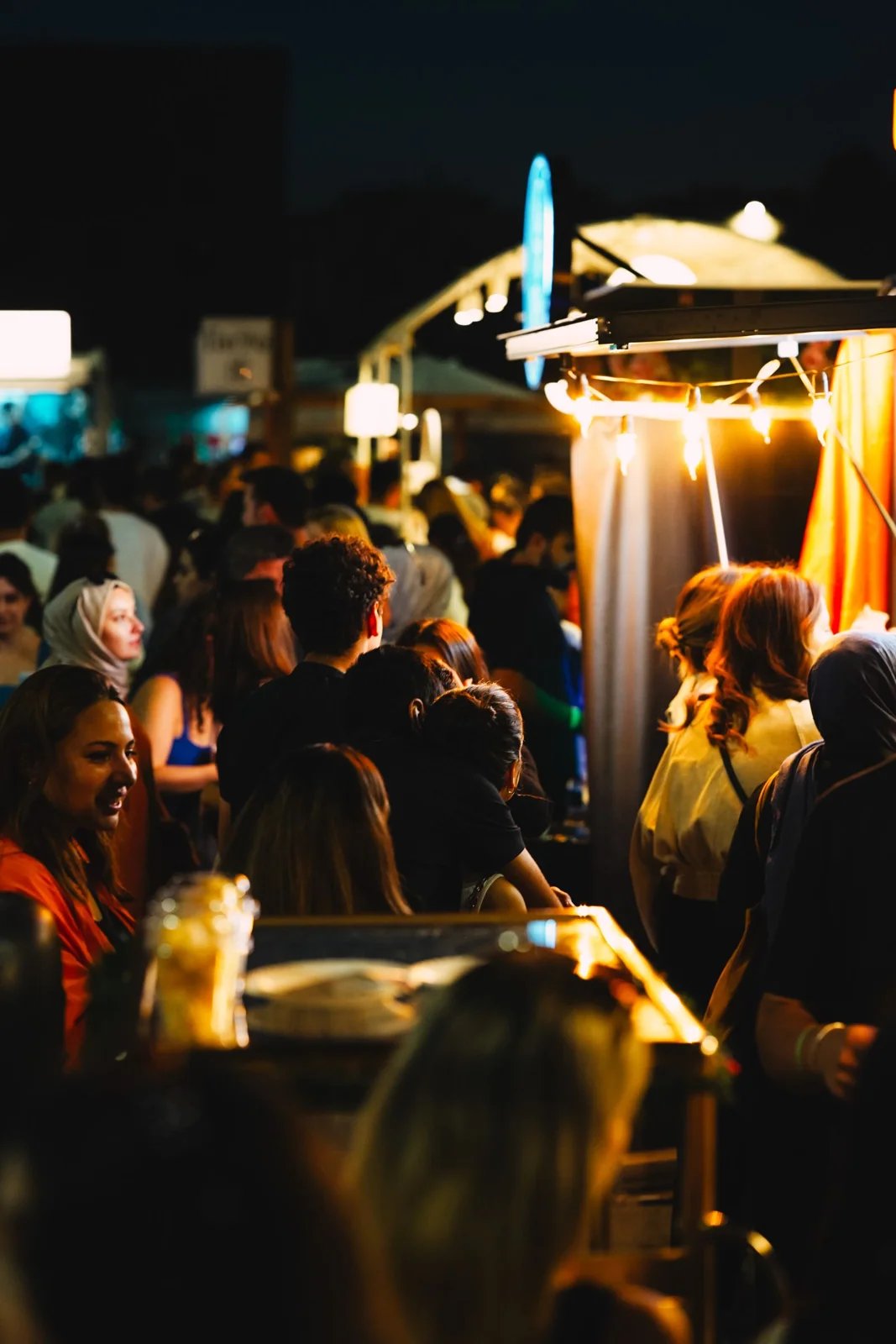 Multitud de noche entre puestos de comida con luces cálidas en un festival