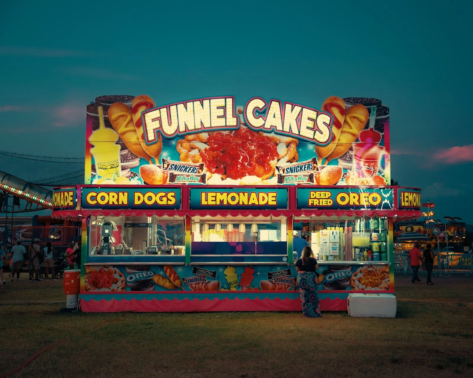 Puesto de feria vendiendo funnel cakes, corn dogs y limonada al atardecer