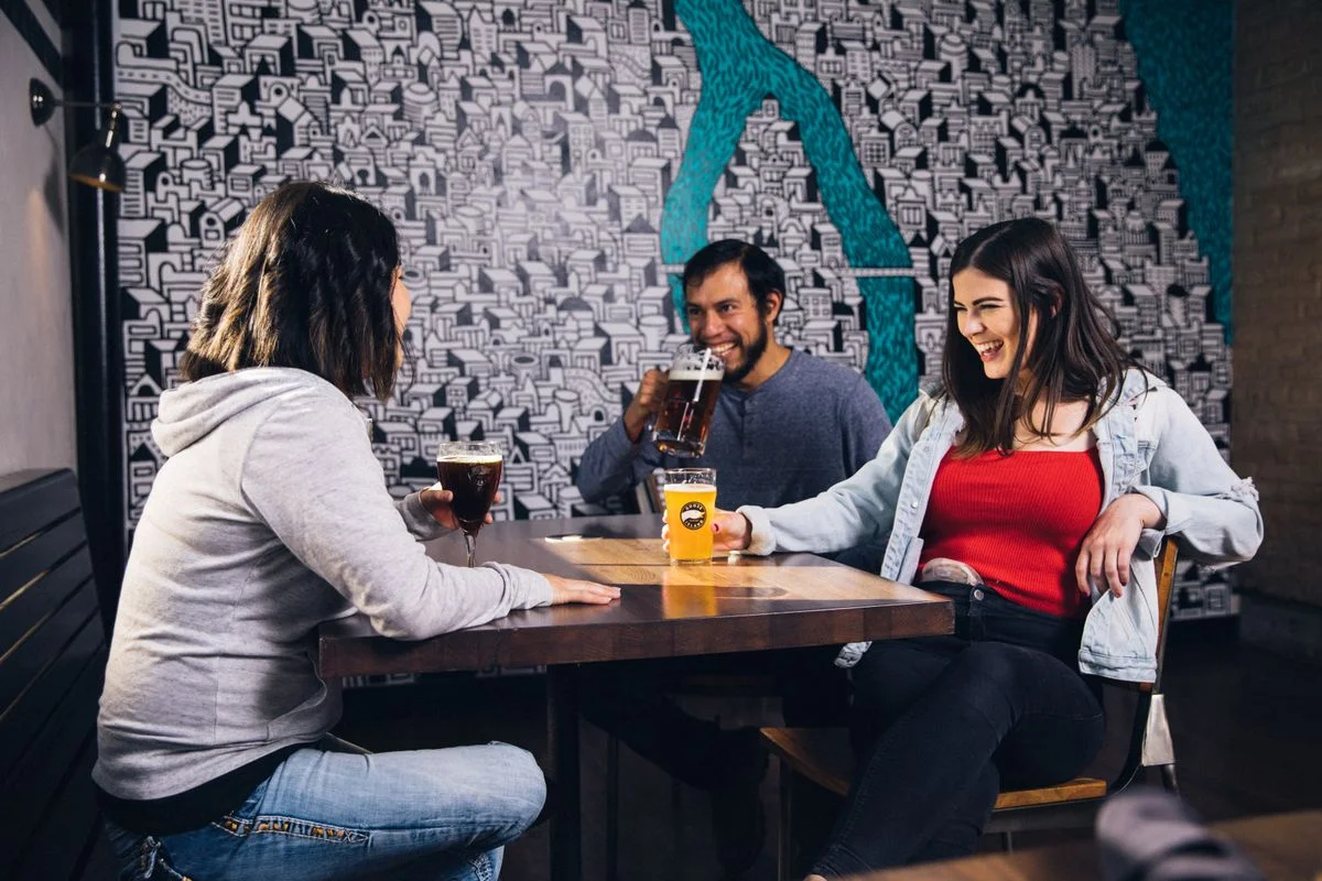 Grupo de amigos riendo alrededor de una mesa con cervezas