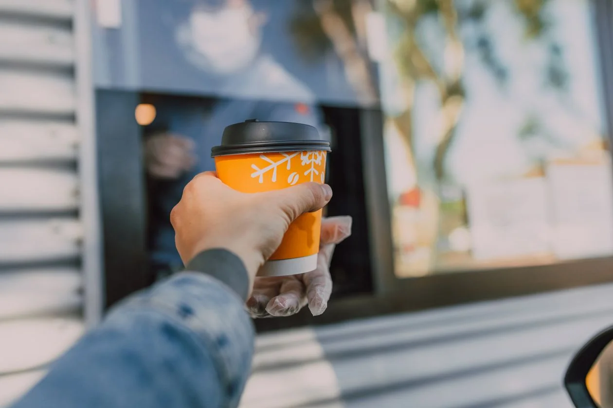 Vaso de café para llevar en la ventana de un carro, estilo drive-thru