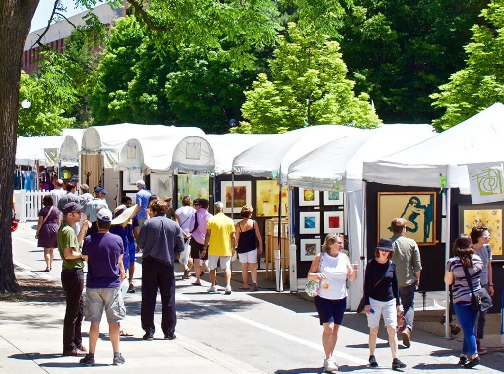 Feria de arte al aire libre con carpas blancas y gente viendo obras