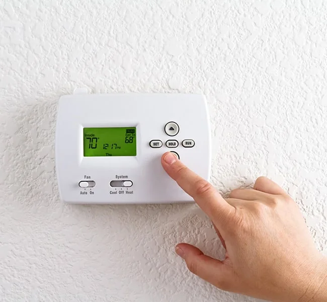 Mano ajustando un termostato en la pared de una casa