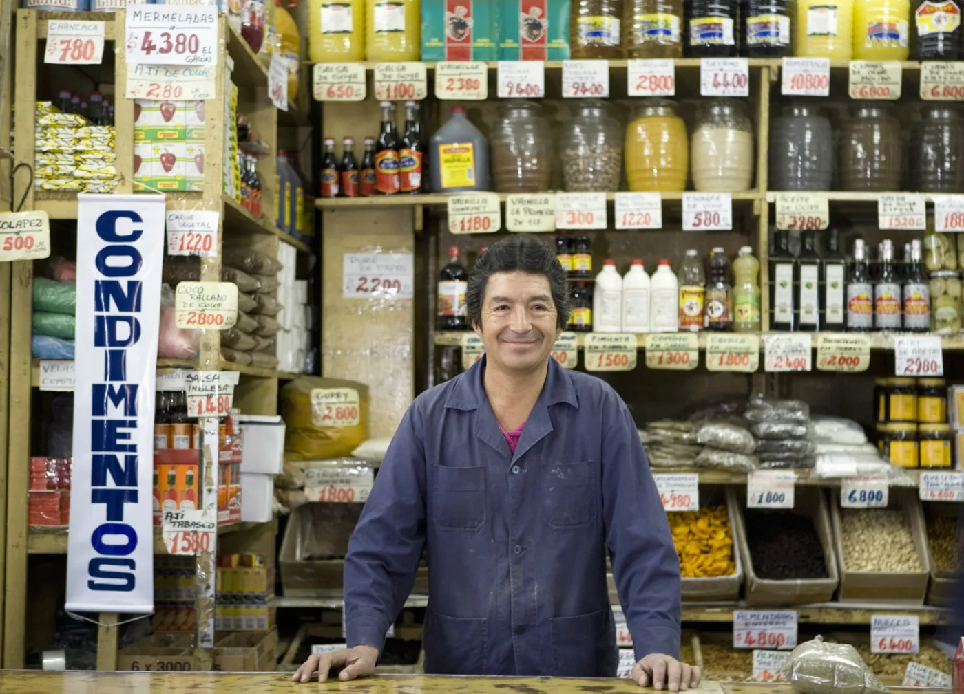 Dueño latino atendiendo su tienda abierta, sonriendo detrás del mostrador