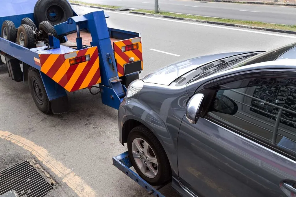 Grúa azul y naranja remolcando un carro gris en la calle de día