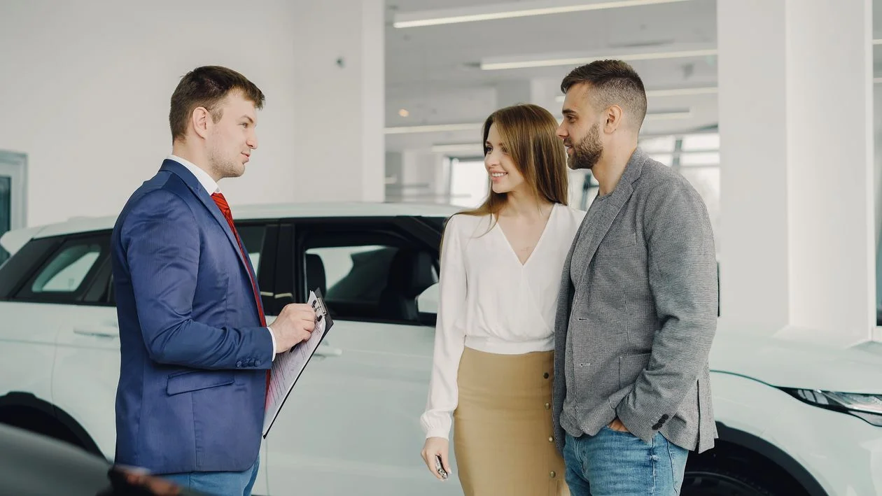 Vendedor mostrando un carro a una pareja en una agencia