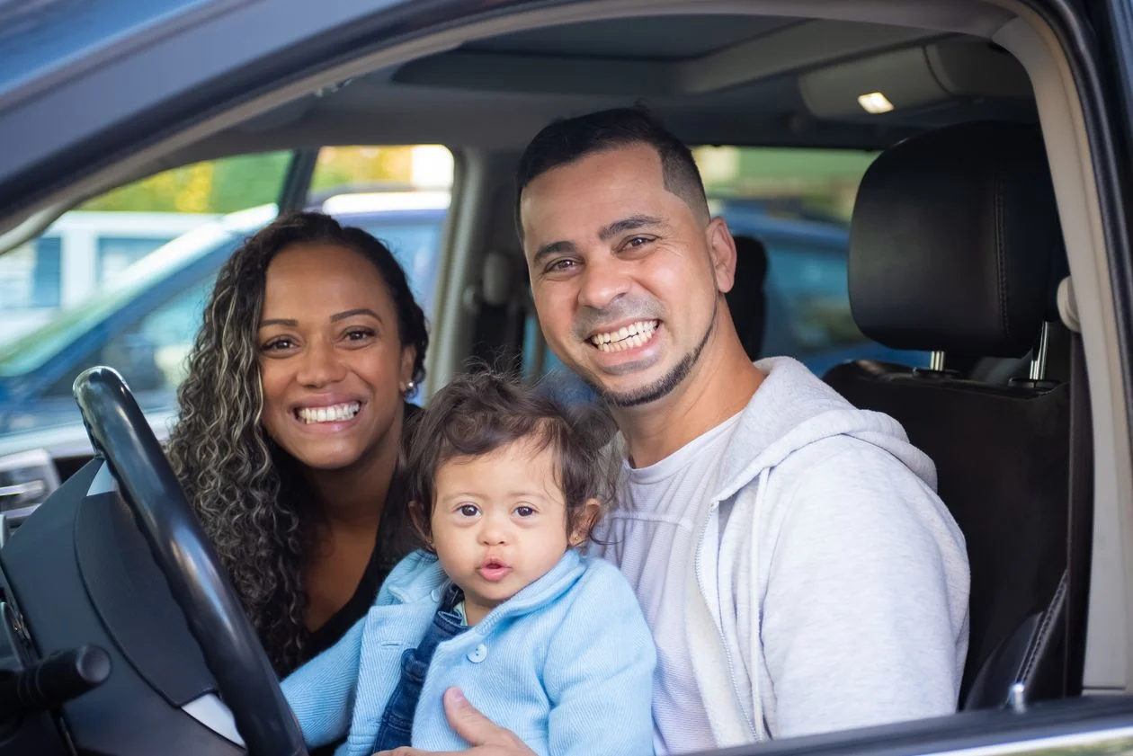 Familia latina sonriendo junto a su carro nuevo