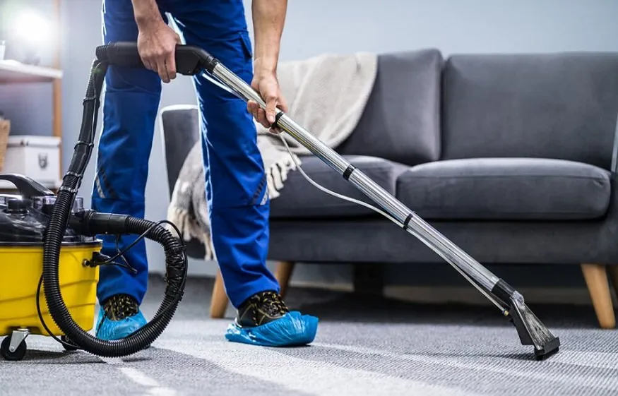 Trabajador limpiando alfombra con máquina extractora en sala de casa