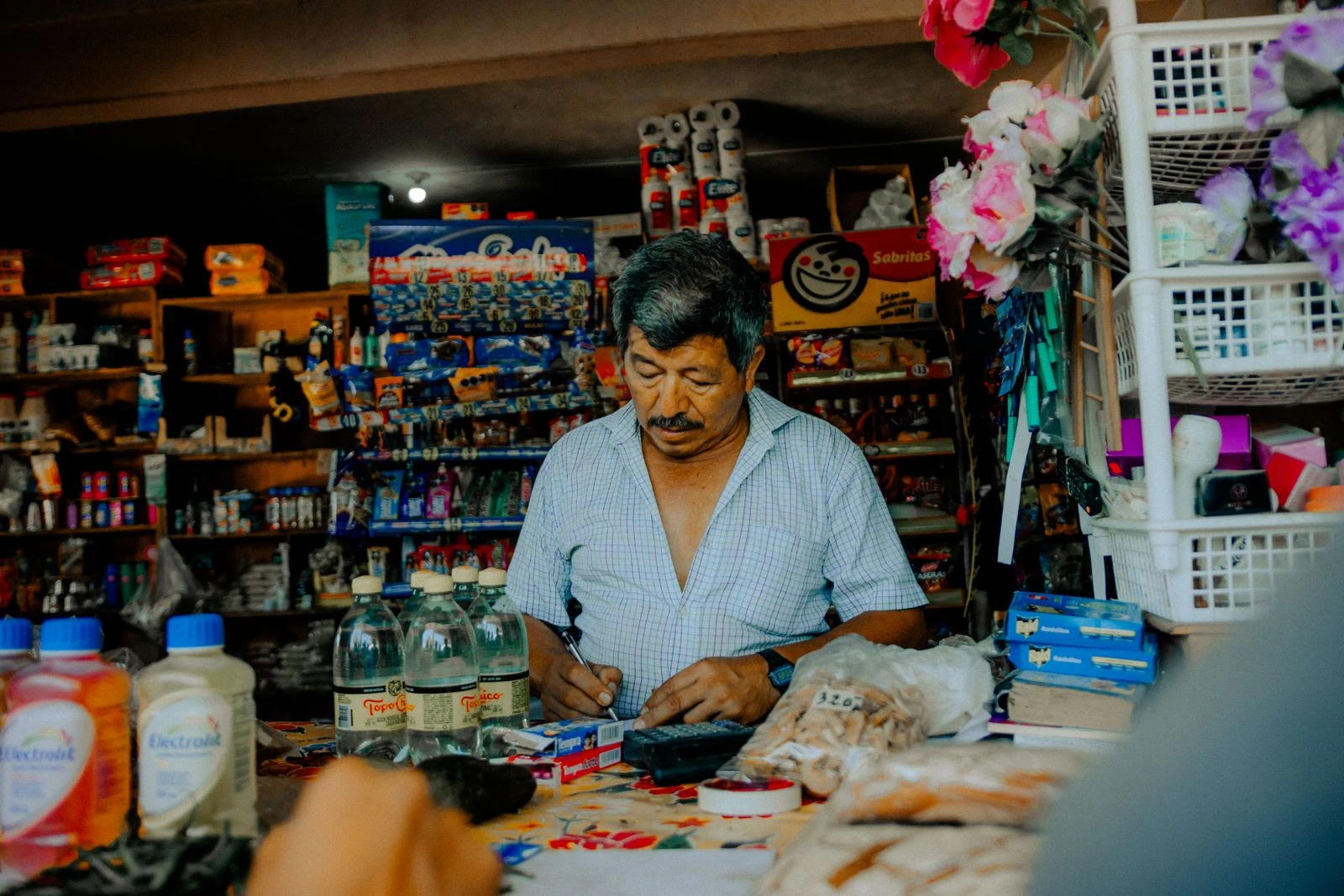 Dueño latino atendiendo detrás del mostrador de su tiendita