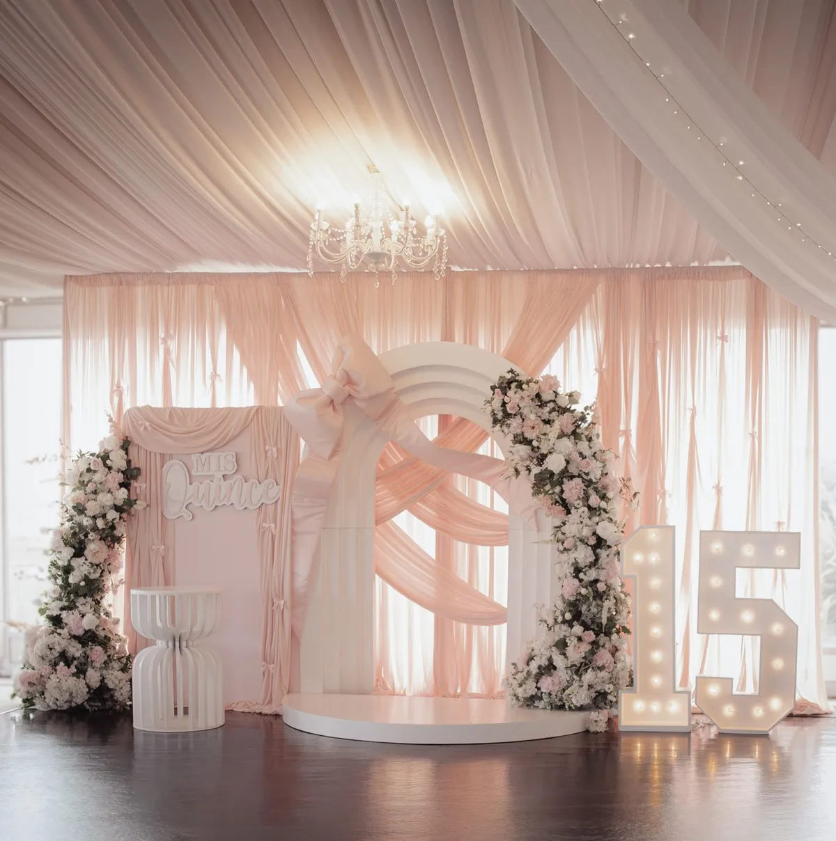 Decoración de quinceañera en rosa con arco de flores y letrero Mis Quince
