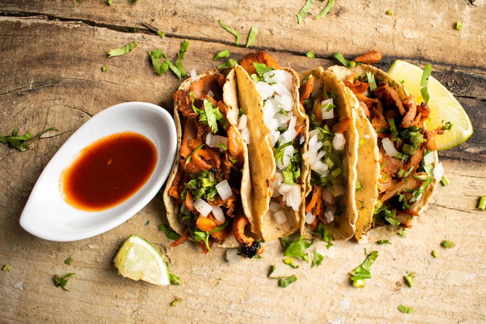 Tres tacos al pastor con cilantro y cebolla servidos con salsa en mesa rústica