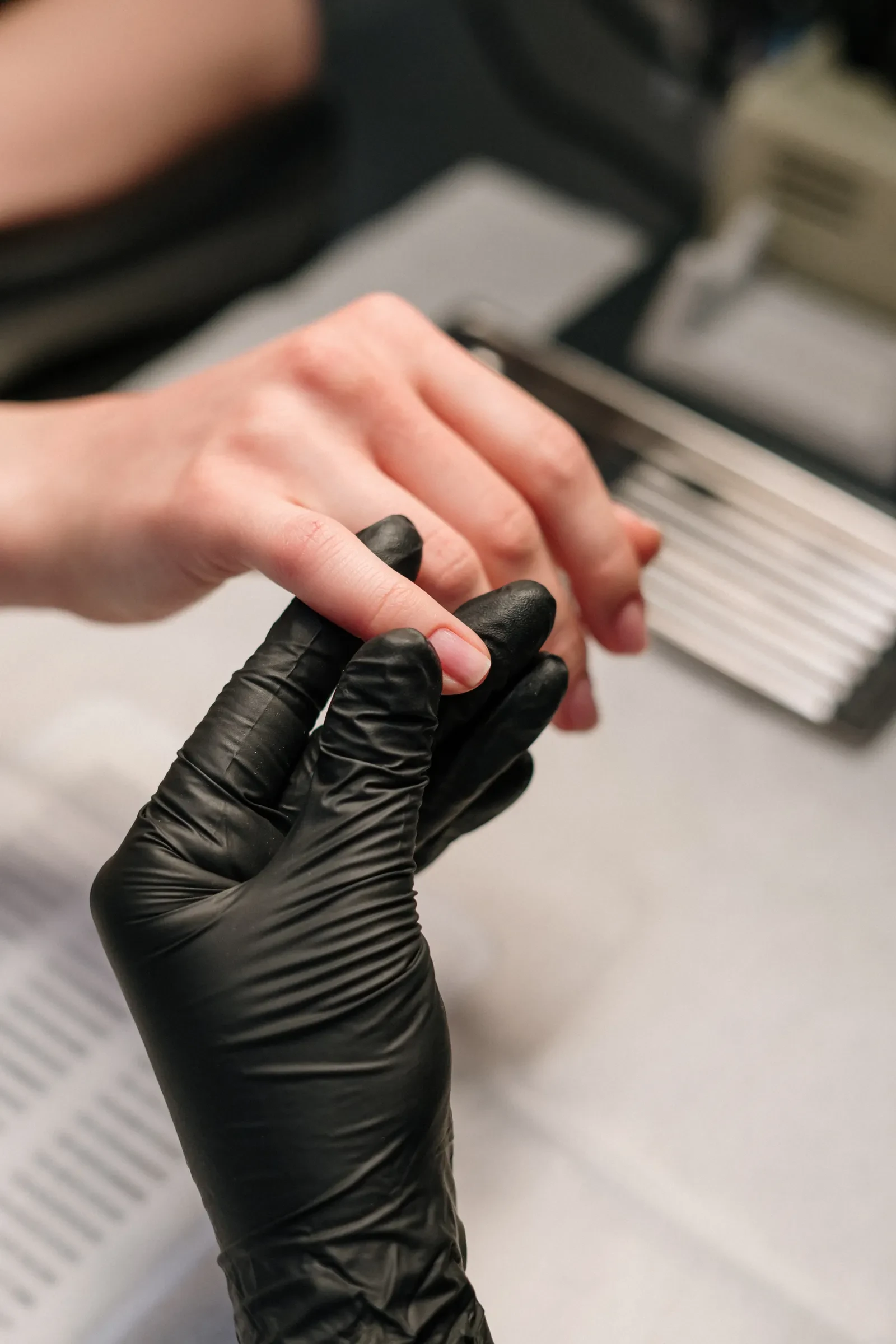 Manicurista con guantes negros trabajando la uña de una clienta