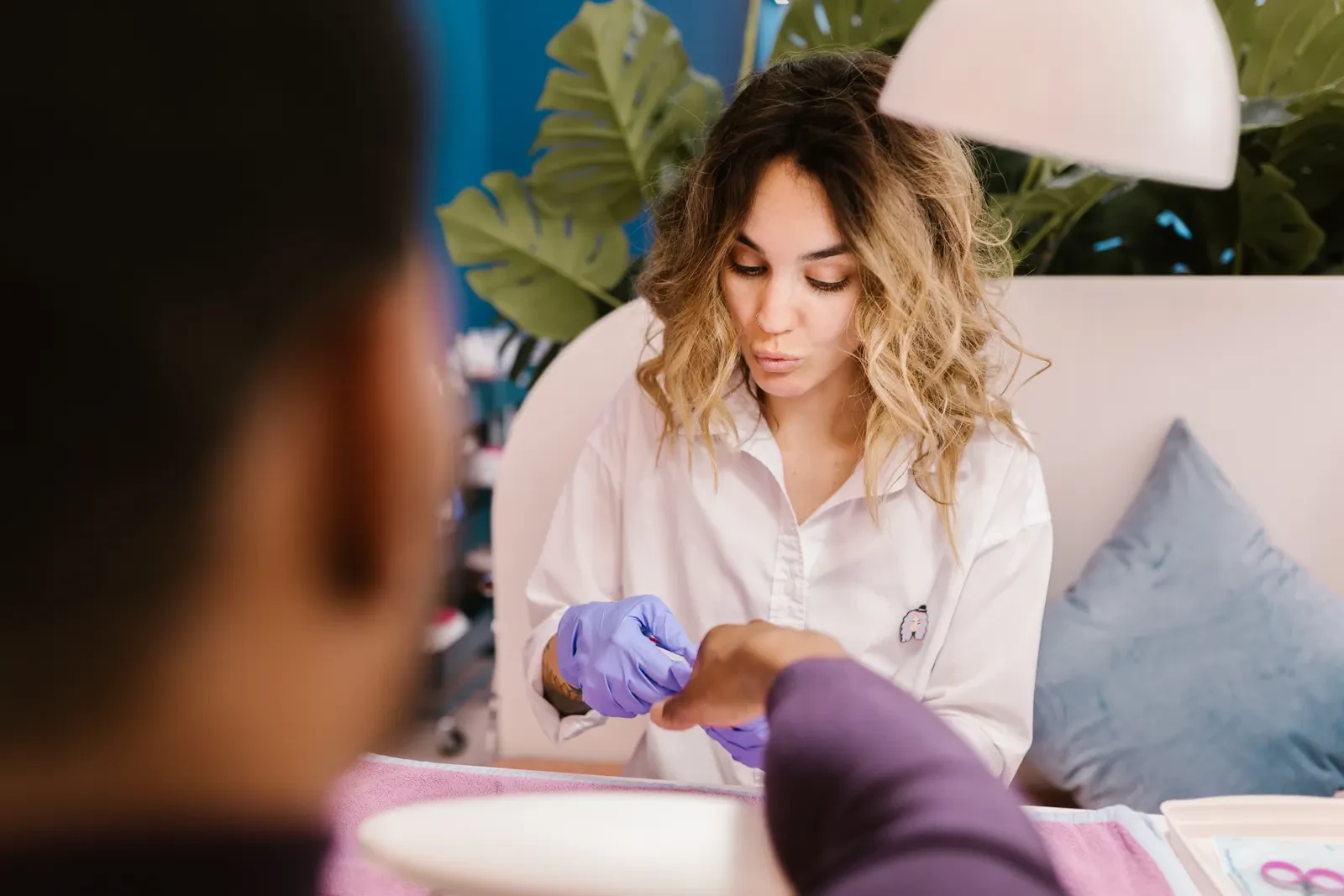Técnica de uñas con guantes atendiendo a una clienta en el salón