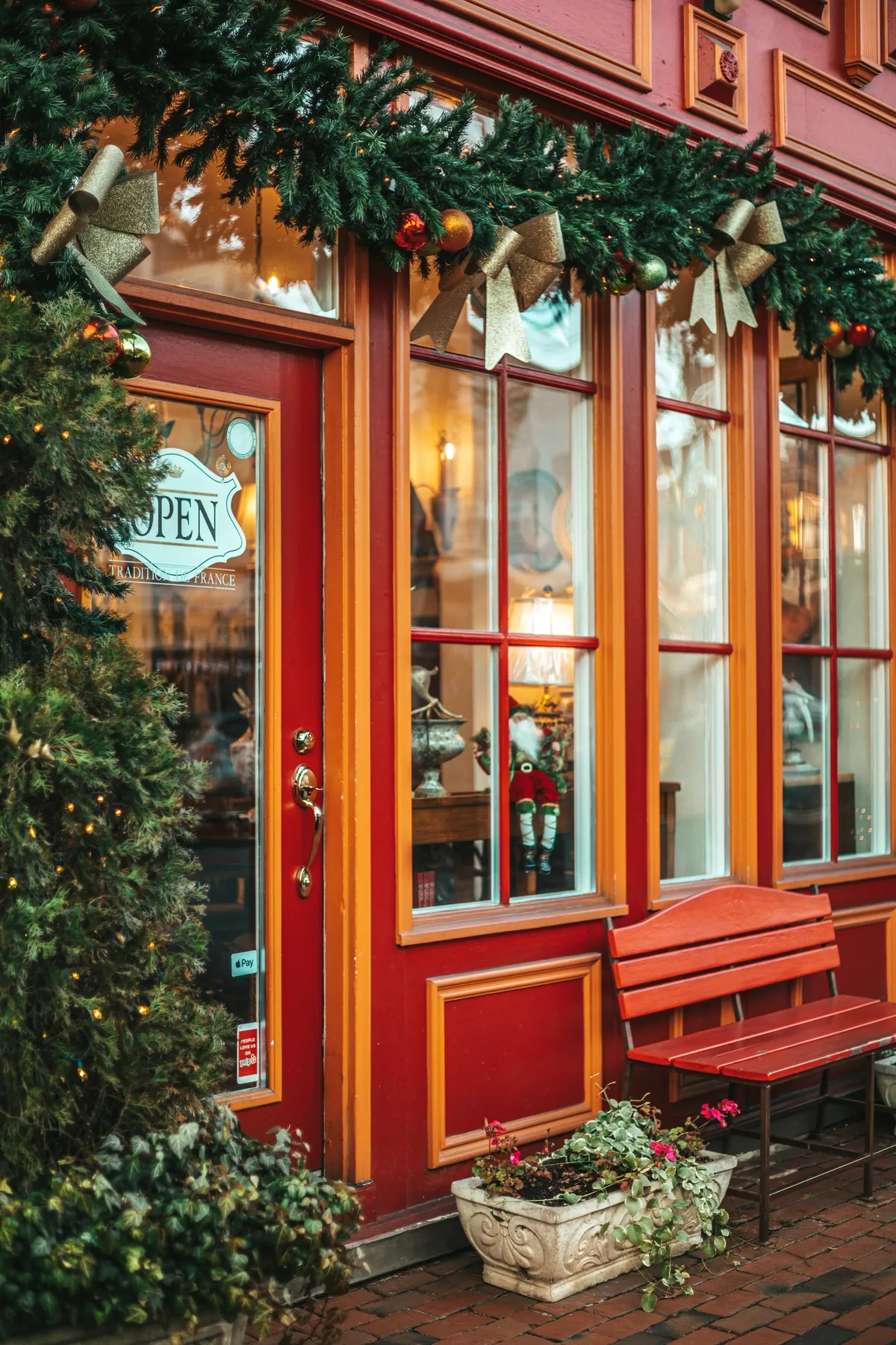 Tienda con fachada roja decorada de Navidad, guirnalda con adornos y letrero de abierto