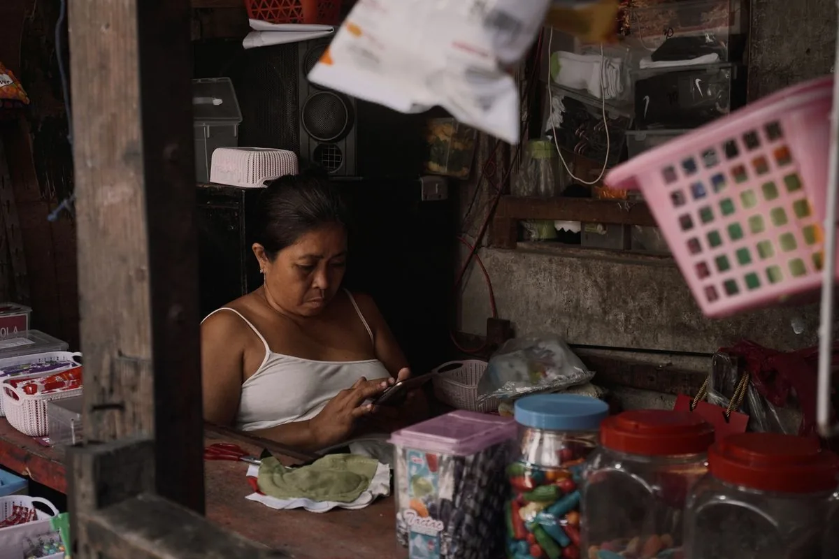 Dueña de tienda de barrio usando el teléfono entre su mercancía