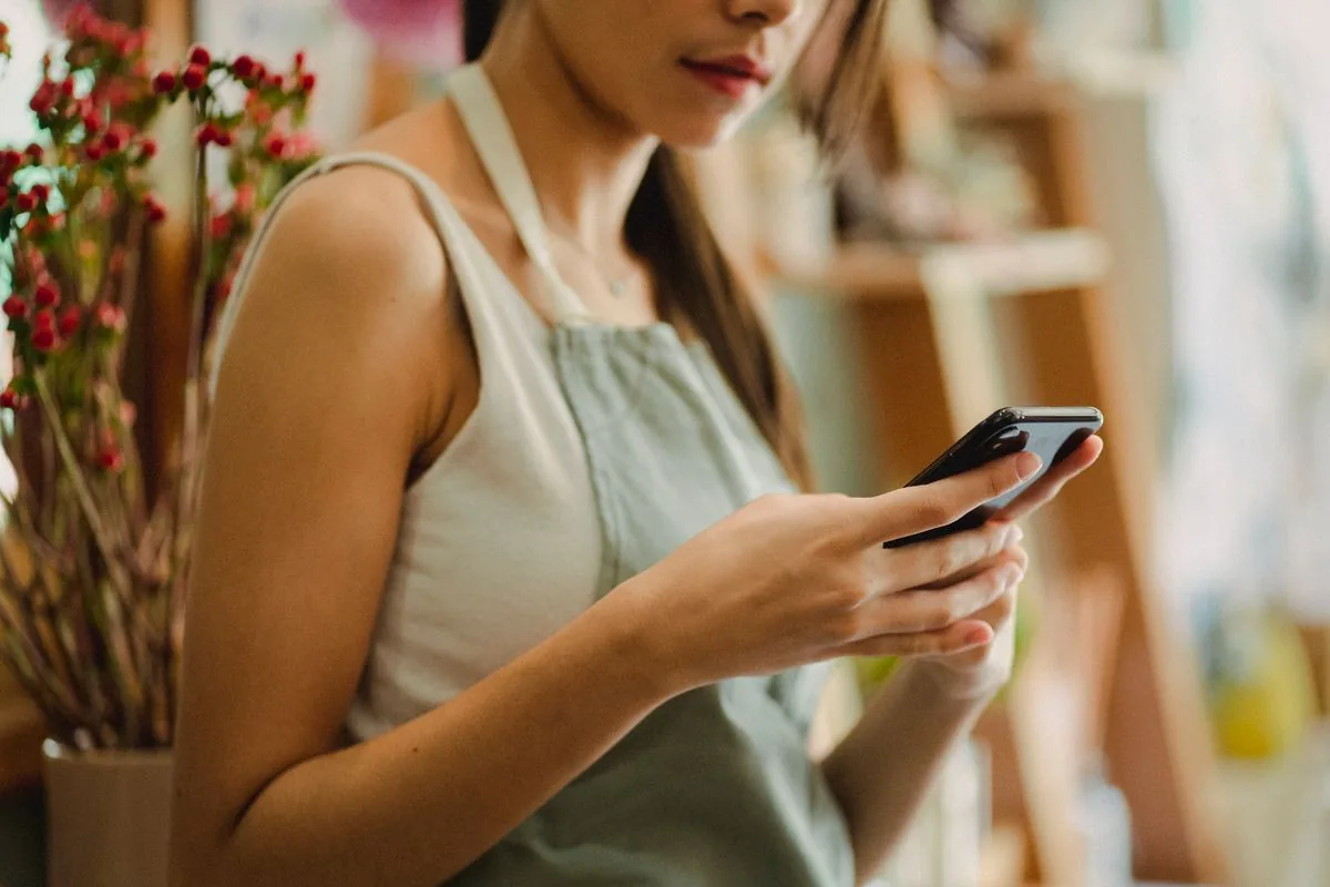 Dueña de florería usando su teléfono en su tienda con luz cálida